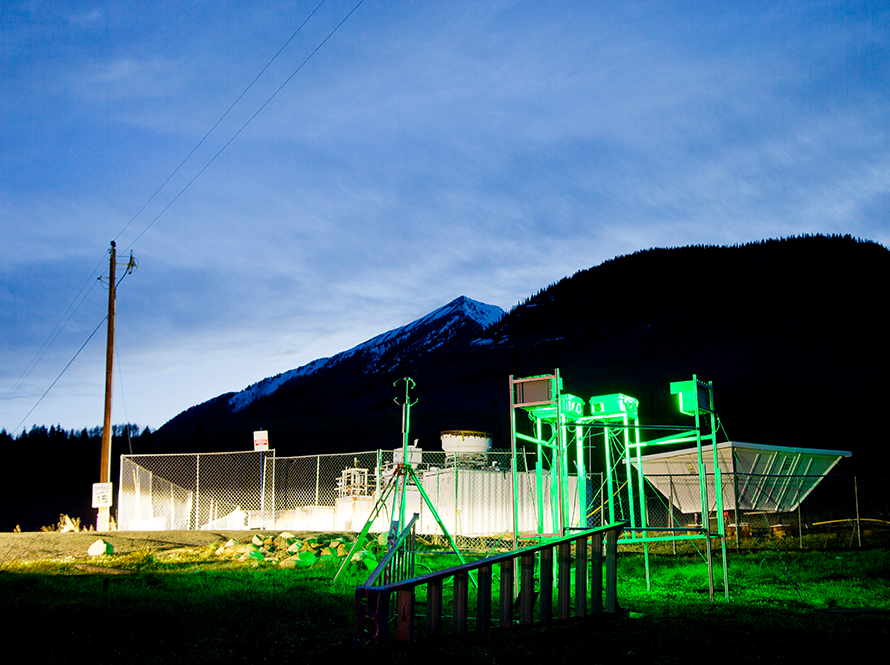 Ground mounted outdoor monitoring equipment bathed in green light at dusk